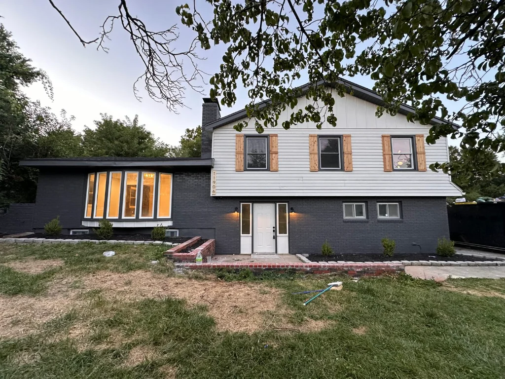 A remodeled split-level home with white siding, charcoal brick, and natural wood shutters
