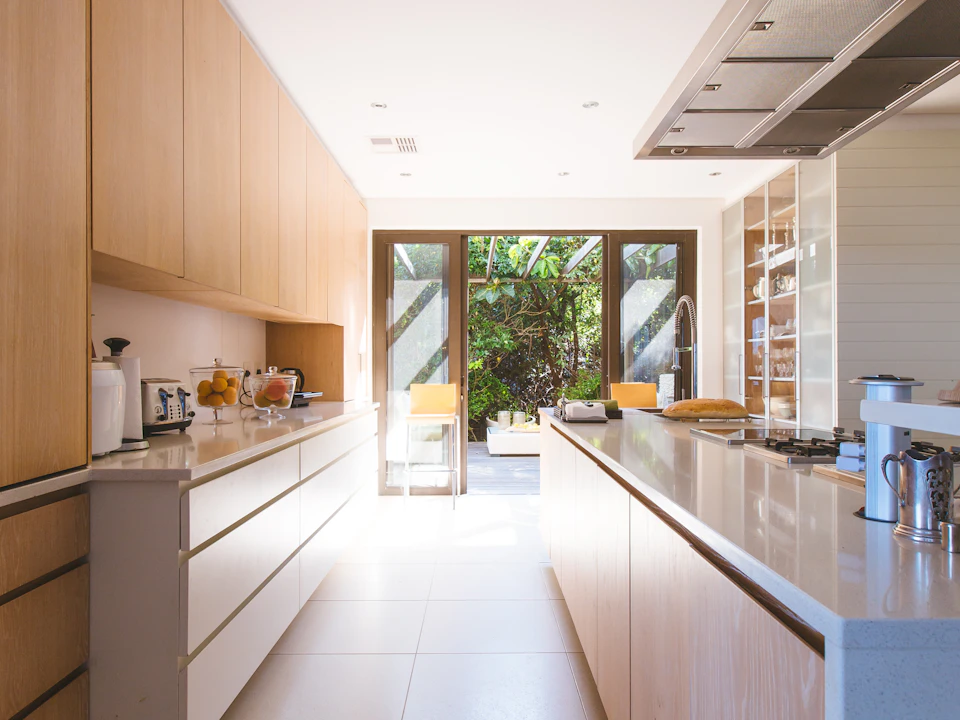 Una cocina luminosa con gabinetes de madera natural y encimeras blancas